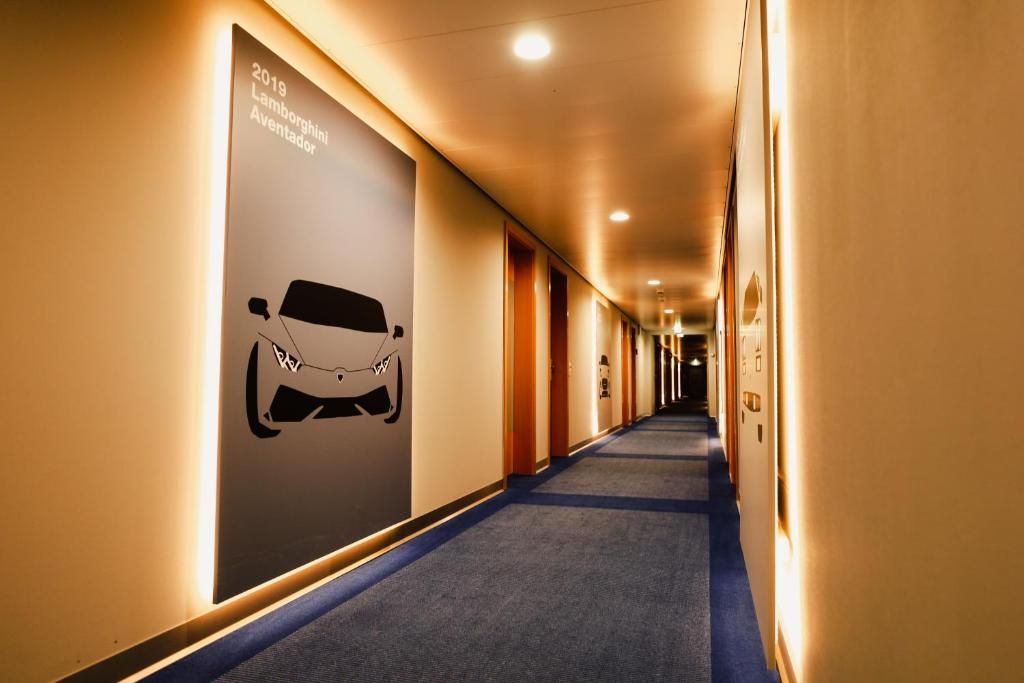 A hotel corridor with a long hallway, illuminated by ceiling lights, and a large poster on the left wall.