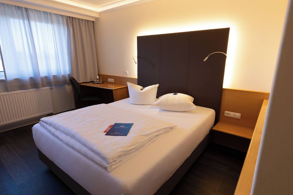 A hotel room with a large bed, a desk, and a chair.