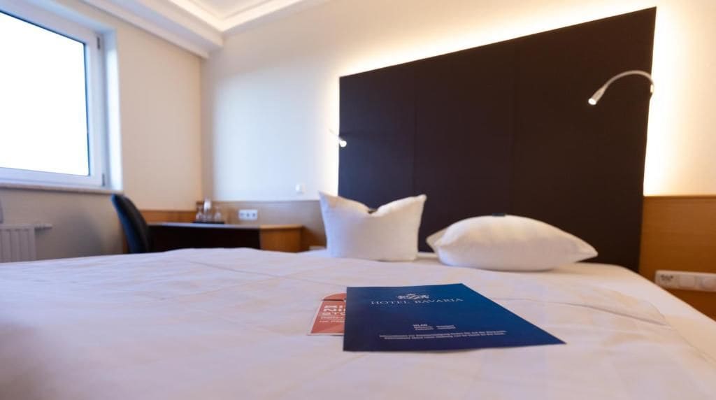 A hotel room with a bed, pillows, a bedside table, and a window.