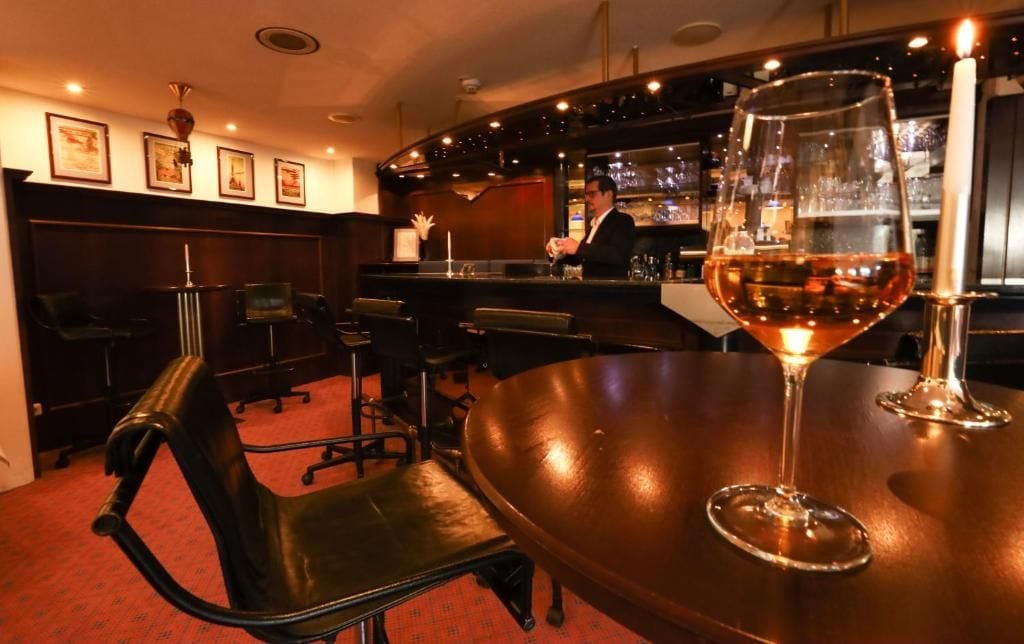 Zona de bar con una mesa redonda, dos sillas, una barra y una copa de vino.