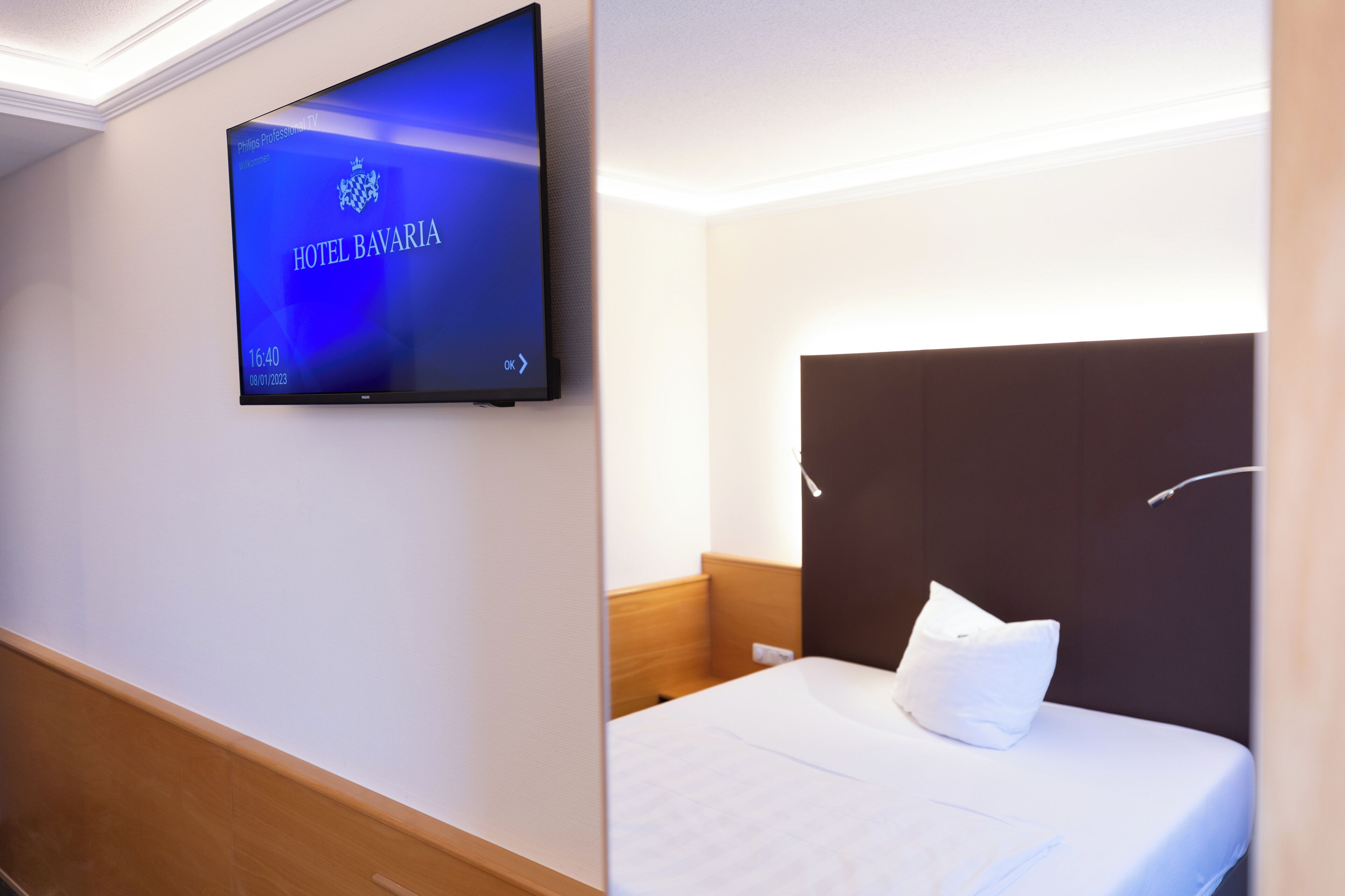 Ein Hotelzimmer mit einem an der Wand befestigten Flachbildfernseher, der den Namen und das Logo des Hotels zeigt.