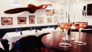Una mesa de comedor con dos copas de vino rosado, una vela y una guitarra colgada en la pared.