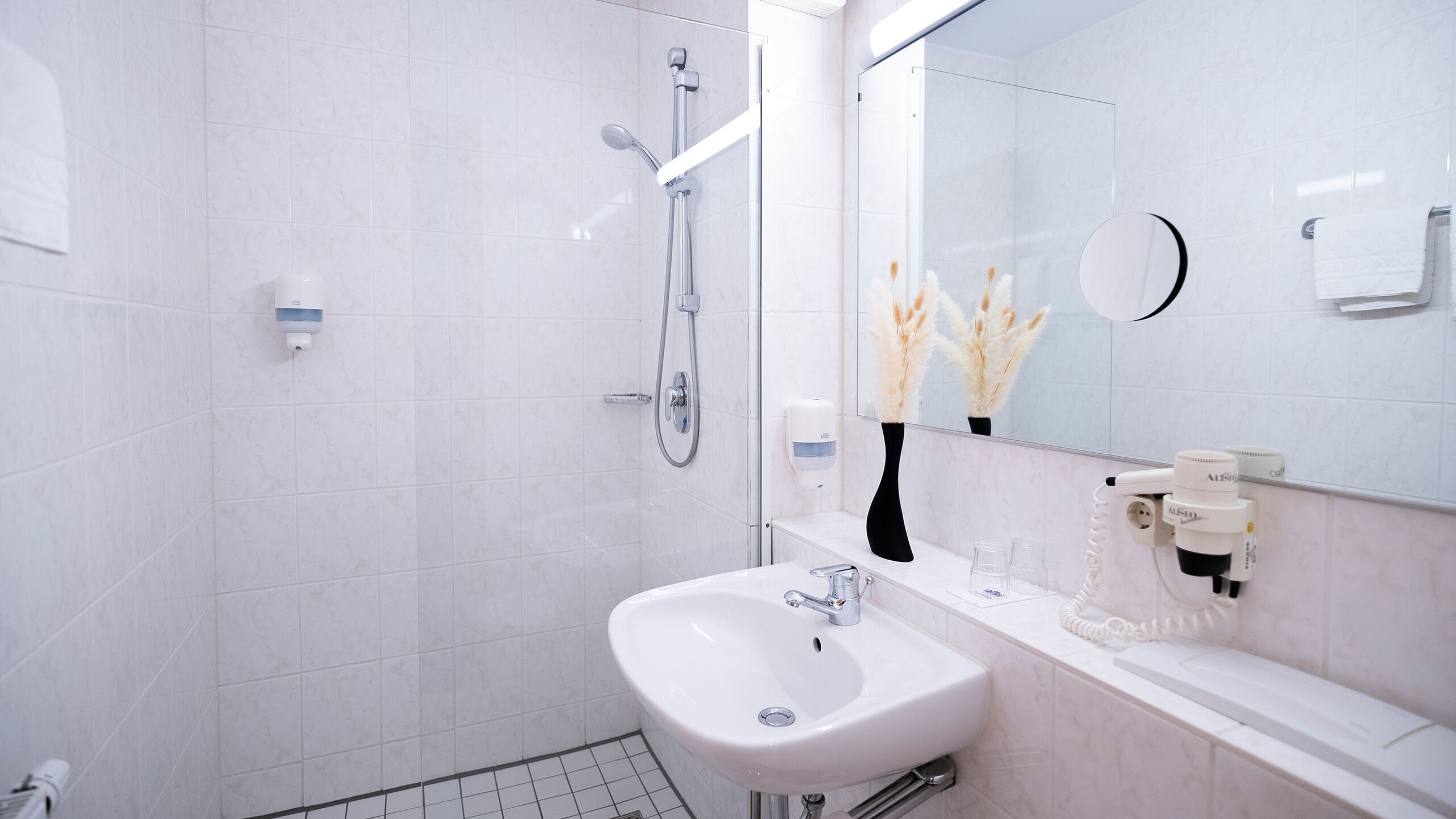 A modern bathroom with a white sink, a glass shower enclosure, and a mirror with a round frame.