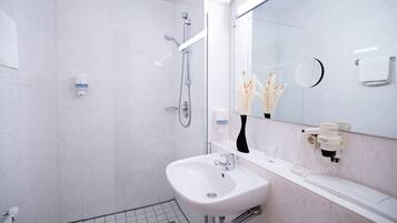 A modern bathroom with a white sink, a glass shower enclosure, and a mirror with a round frame.