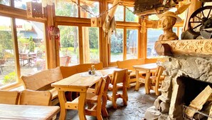A rustic wooden interior with stone flooring, wooden tables and benches, and a fireplace with logs. - Zajazd Białczański (Bukowina Tatrzanska)