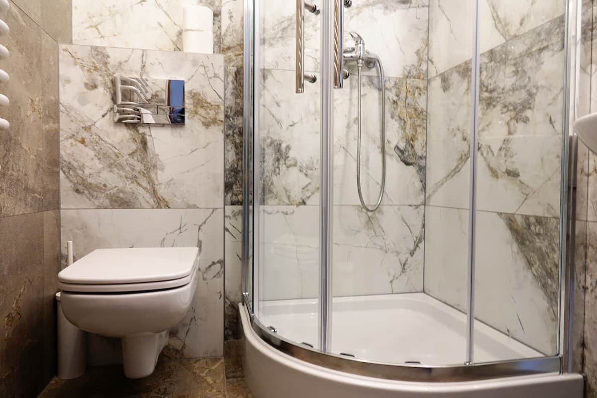 Un baño con ducha de vidrio, inodoro y paredes de mármol.
