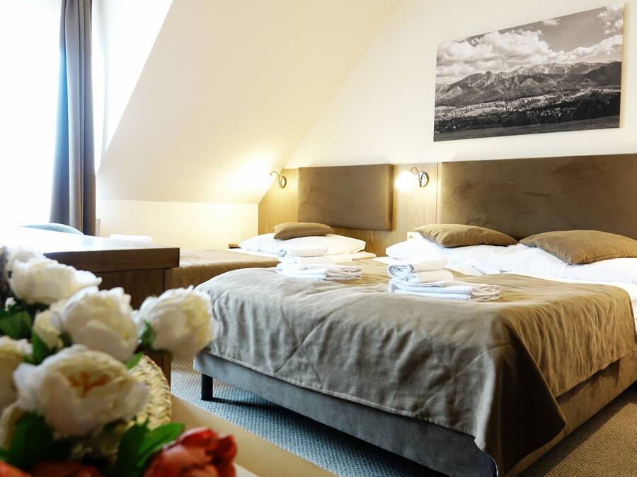 A hotel room with a bed, bedside tables, a nightstand, a wall-mounted picture, and a window with curtains.
