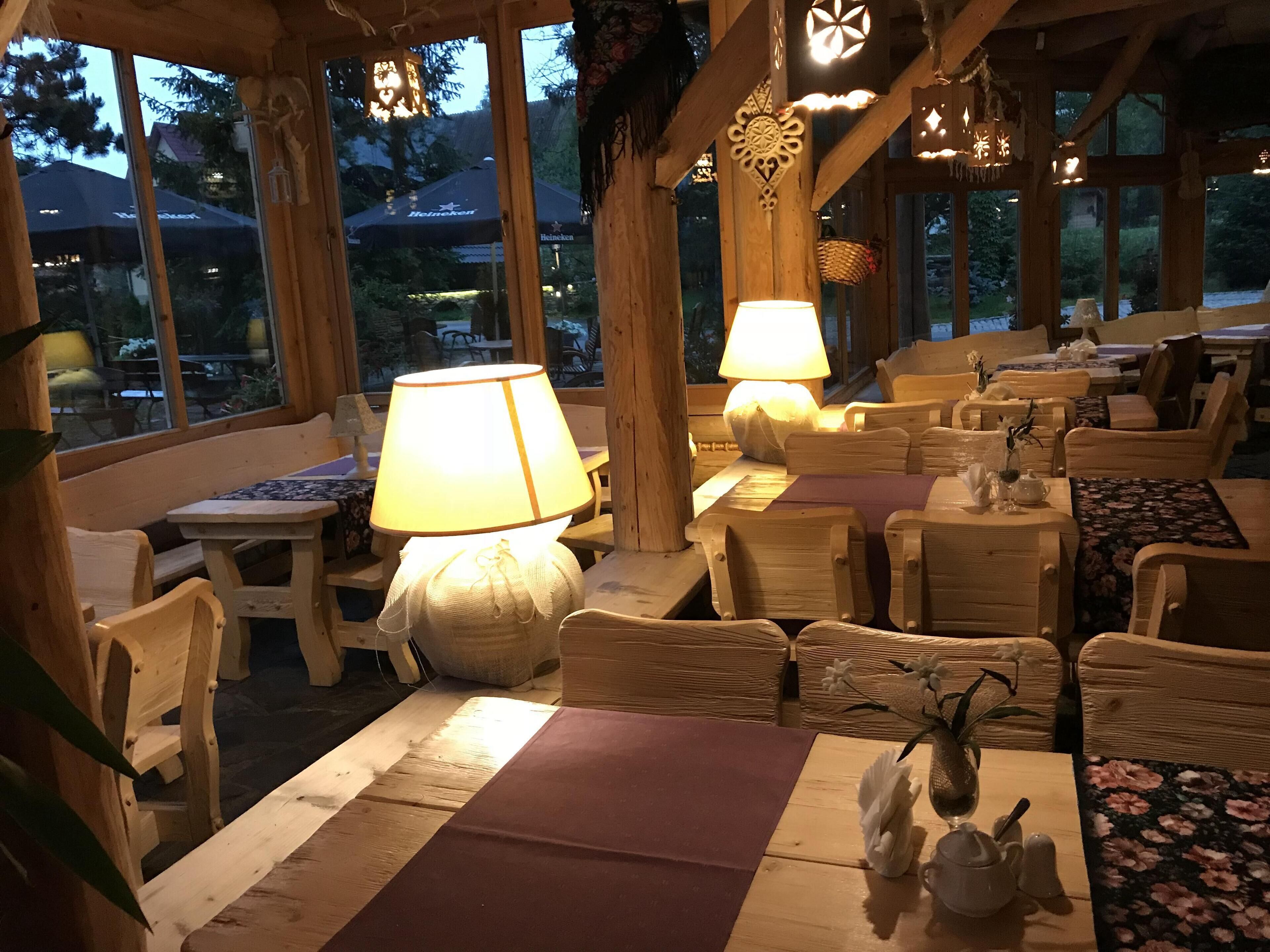 Un espace de restauration intérieur avec des meubles en bois, des tables recouvertes de nappes et des luminaires suspendus.