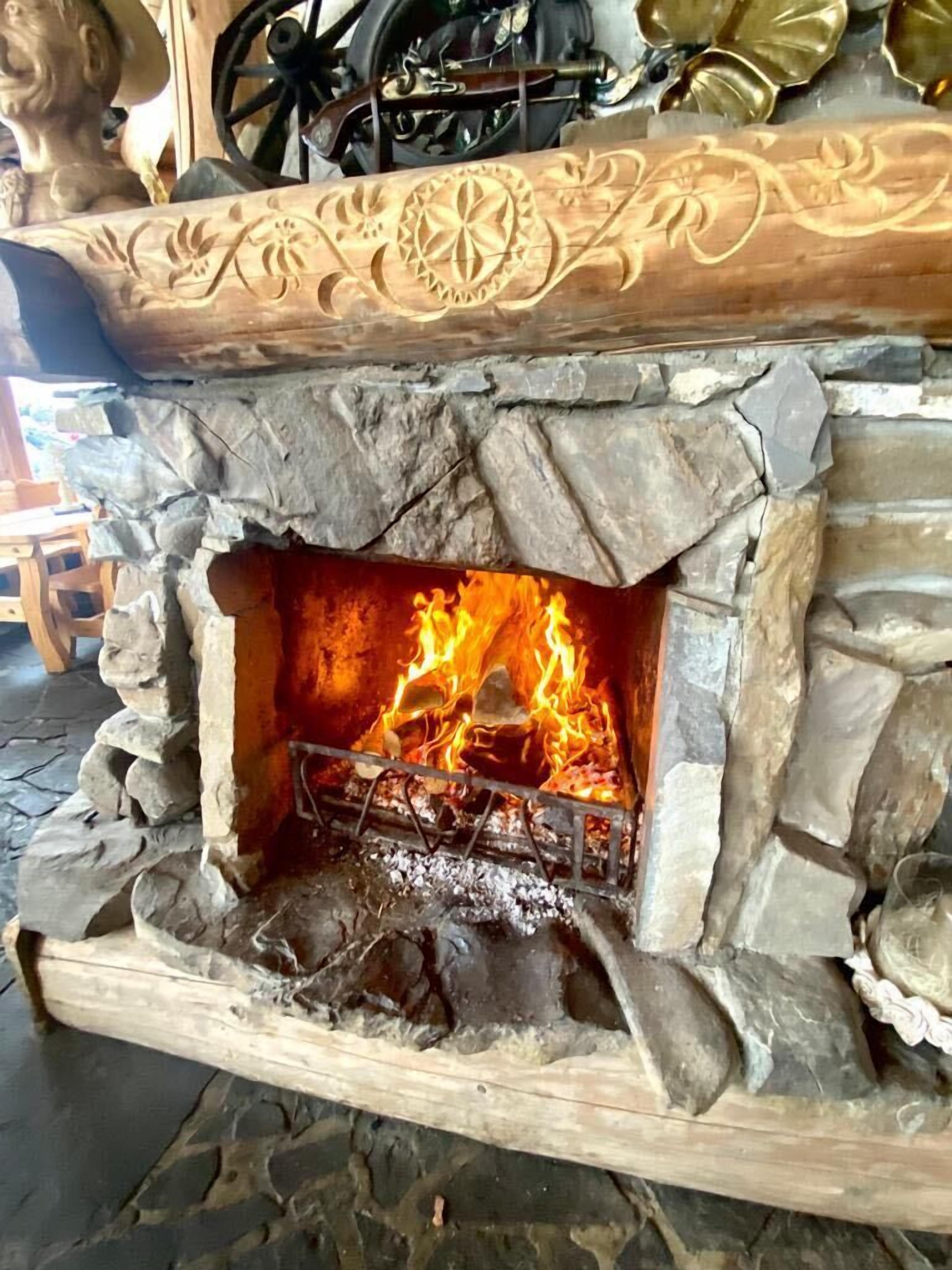 A stone fireplace with a fire burning inside, surrounded by a rustic stone wall.