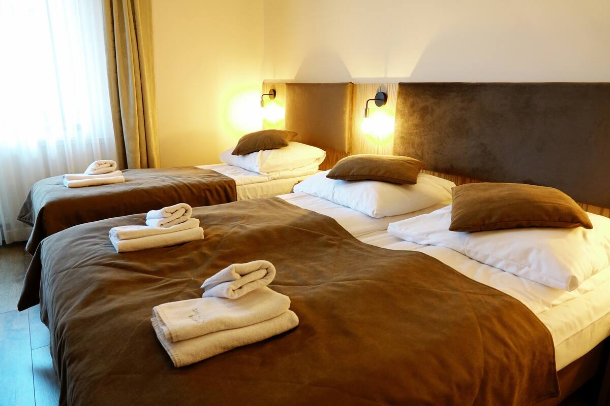 Habitación de hotel con dos camas, cada una con cubrecama marrón, ropa de cama blanca y almohada marrón. Hay dos lámparas de pared a cada lado de las camas.