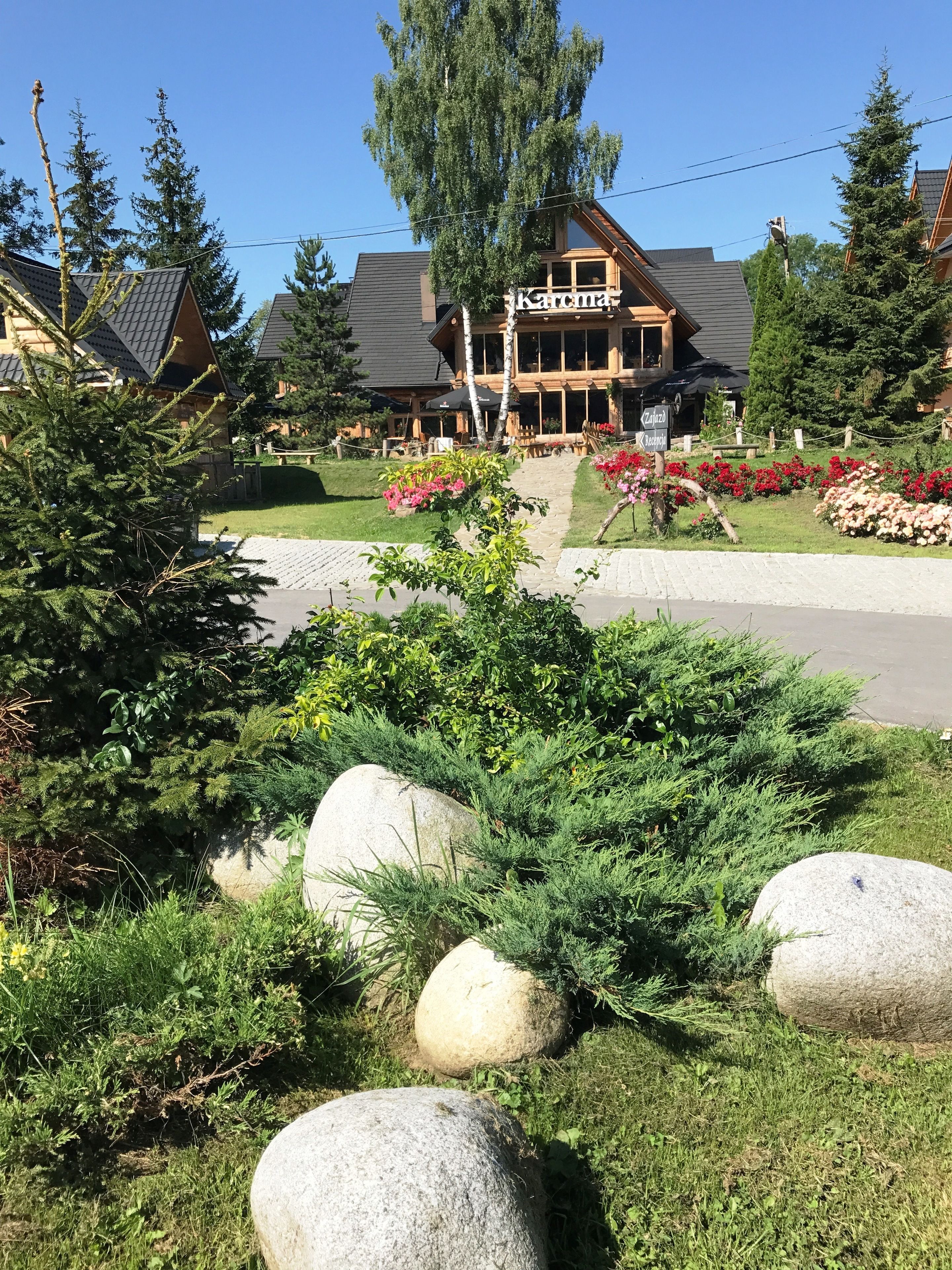 Un chalet doté d’un grand bâtiment en bois, d’un espace extérieur aménagé pour s’asseoir et d’un jardin bien entretenu avec des rochers et des arbustes.