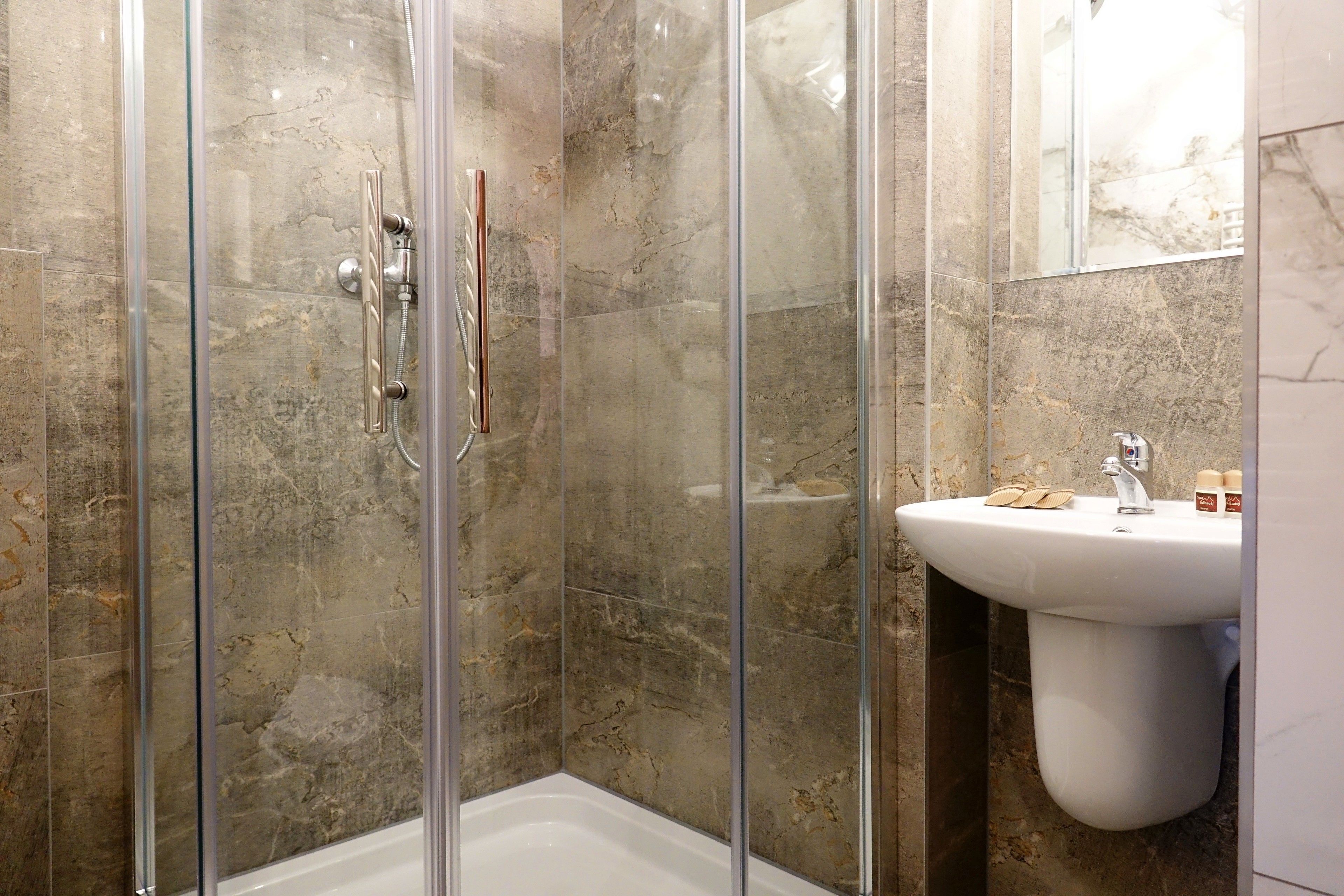 A modern bathroom with a glass-enclosed shower, a white sink, and marble walls.