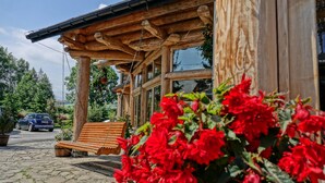A wooden building with a stone-paved entrance, a wooden bench, and red flowers in the foreground. - Zajazd Białczański (Bukowina Tatrzanska)