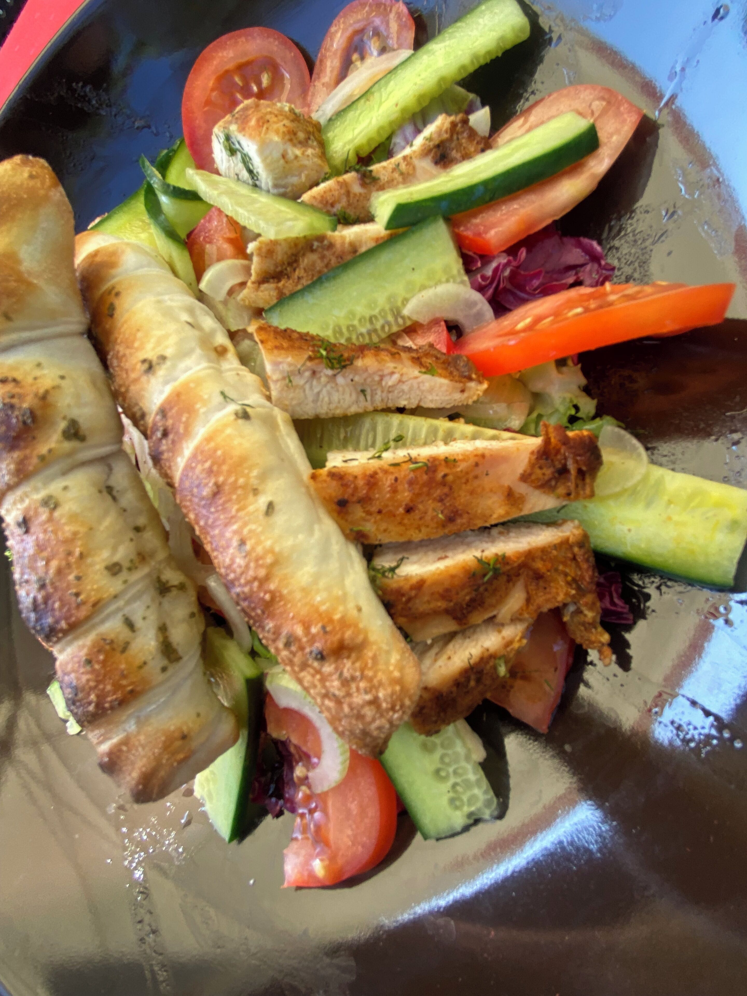 A meal with grilled chicken, vegetables, and a bread roll on a plate.