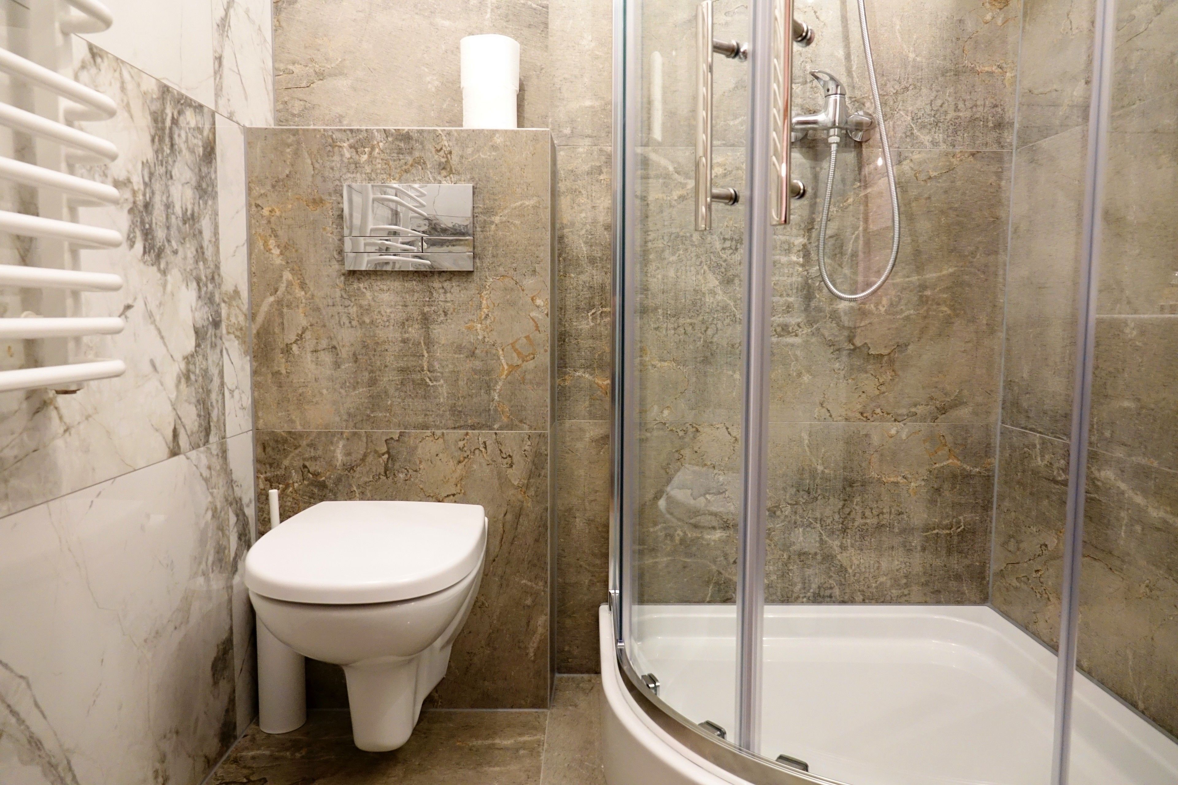 A bathroom with a toilet, a shower enclosure, and a marble-tiled wall.