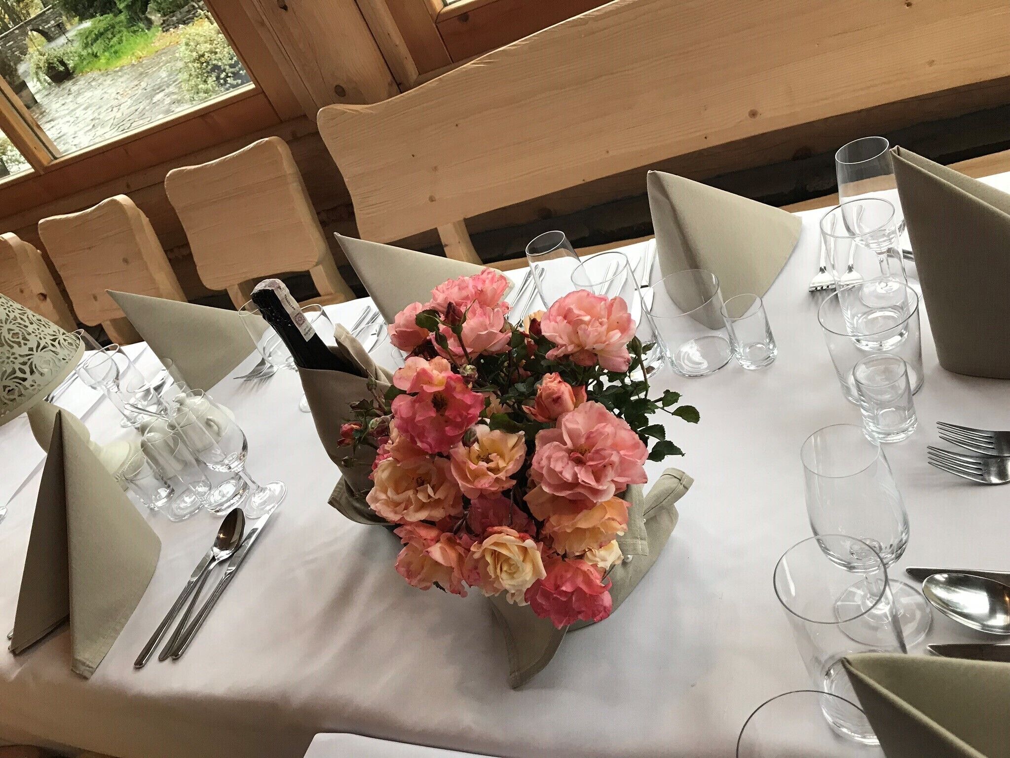 Une table mise pour un repas, agrémentée d’un centre de table composé de fleurs roses, de verres transparents et de couverts disposés avec soin.