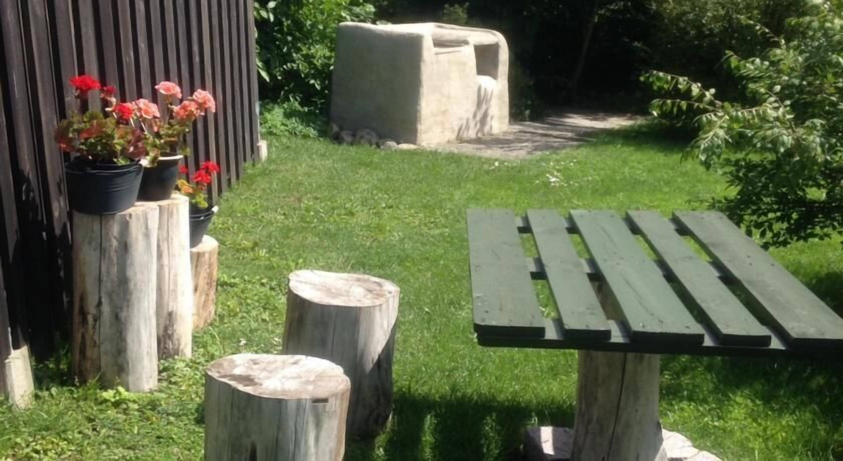 Un banco de madera y una mesa pequeña en un jardín con un cerco de madera y plantas en macetas.