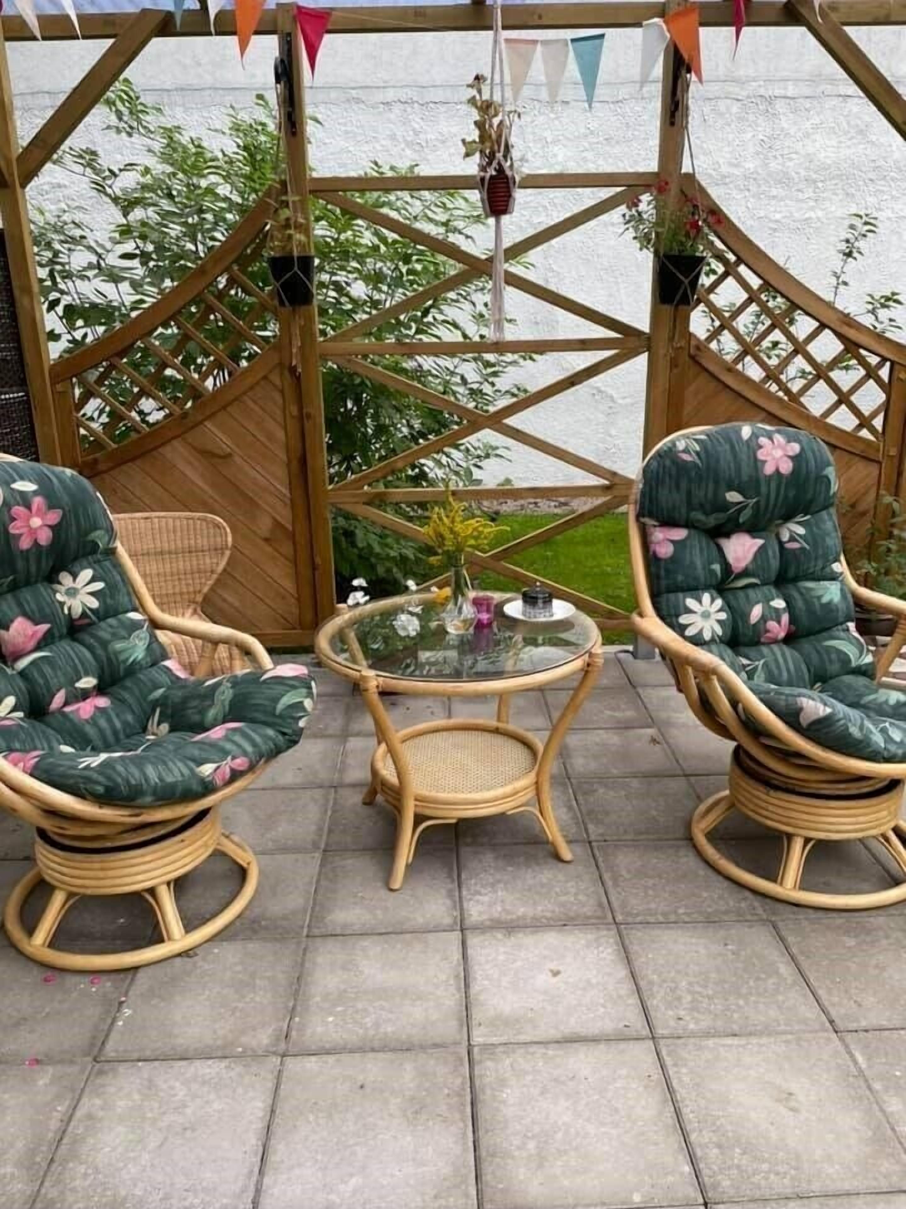 A covered outdoor seating area with wicker chairs and a glass table, surrounded by a wooden lattice structure.