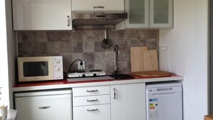 Una cocina compacta con microondas, tostadora, lavamanos y tabla de cortar de madera.