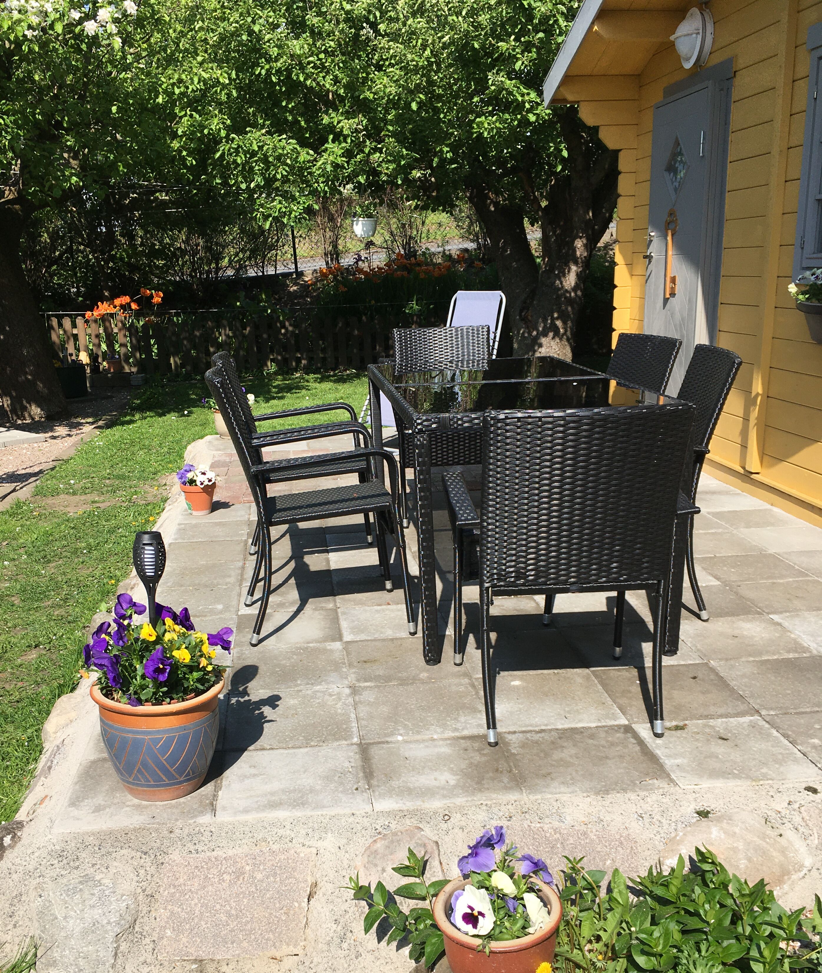 Patio esterno con tavolo e sedie, circondato da piante in vaso e un giardino.