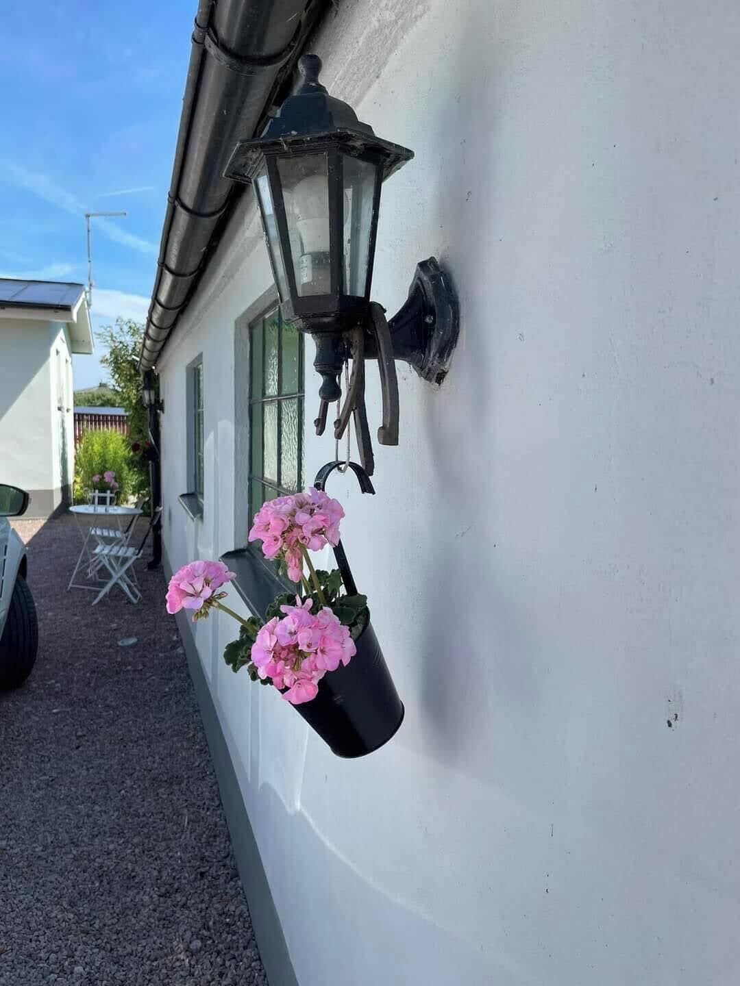 Un edificio blanco con un aplique negro montado en la pared y una maceta colgante con flores rosas.