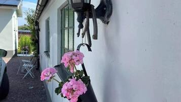 Un edificio blanco con un aplique negro montado en la pared y una maceta colgante con flores rosas.