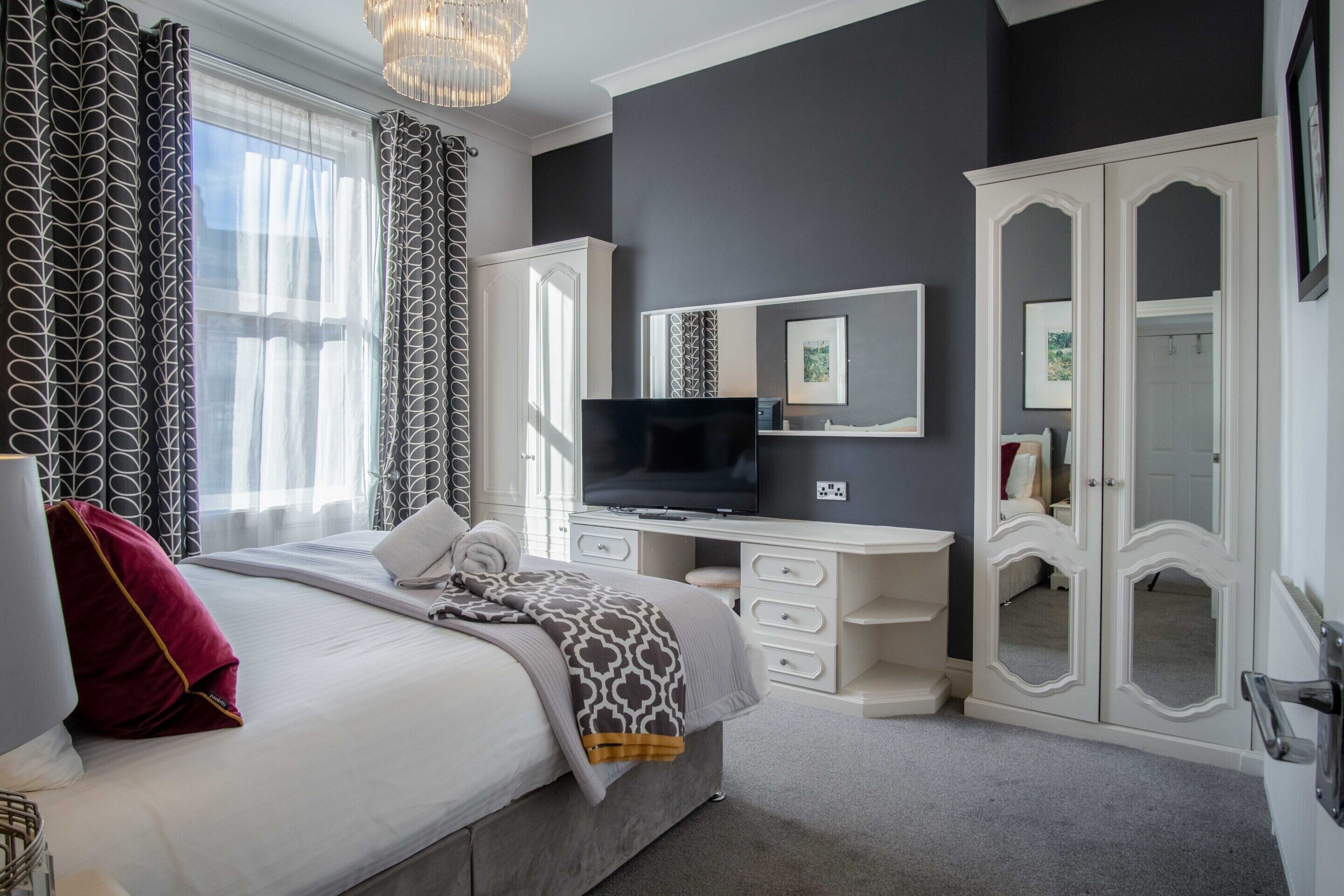 Een slaapkamer met een bed, een bureau, een televisie en een kledingkast.