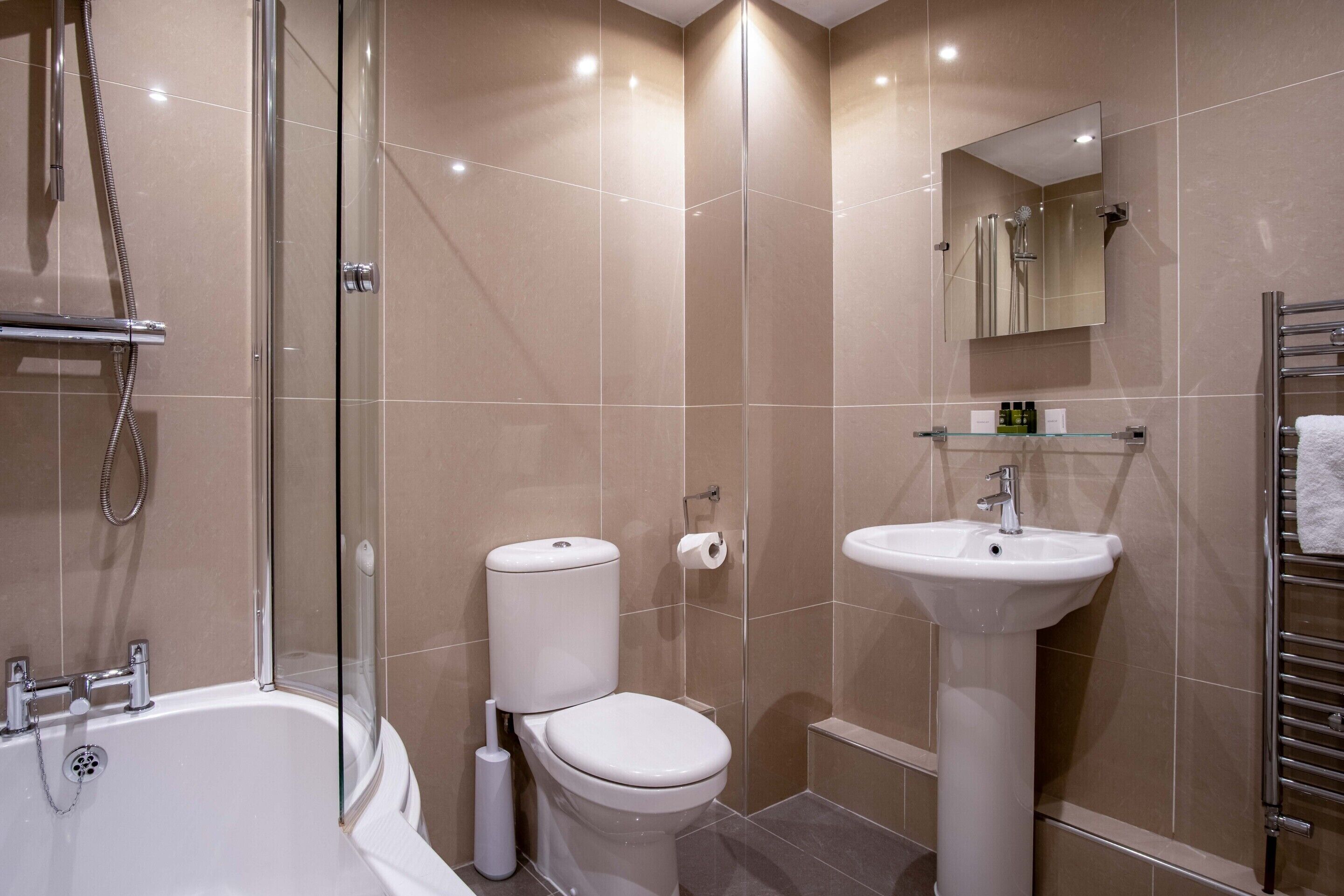 A modern bathroom with a glass-enclosed shower, a white toilet, and a pedestal sink.