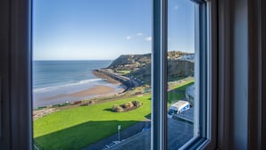 A coastal view from a window overlooking a beach, grassy areas, and a rocky cliff. - Blue Horizon Apartments at The Helaina (Scarborough)
