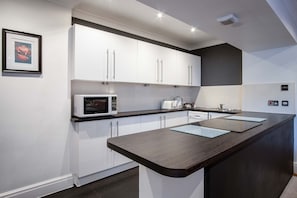 Une cuisine moderne avec des meubles blancs, un plan de travail foncé et un four à micro-ondes.