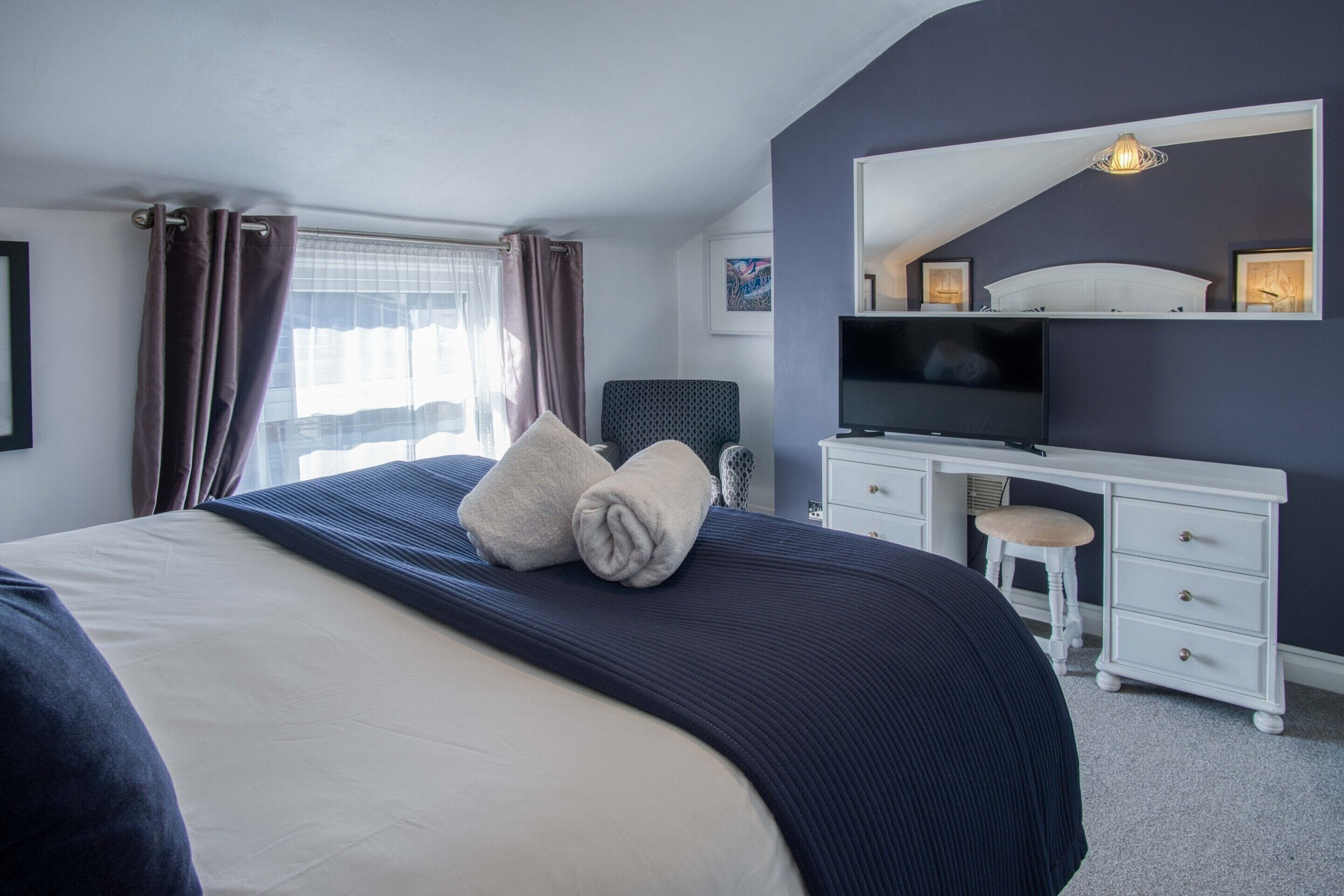 Ein Hotelzimmer mit einem großen Bett, einem Schreibtisch mit Fernseher und einem Fenster mit Vorhängen.
