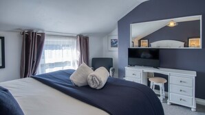 Ett hotellrum med en stor säng, ett skrivbord med en tv och ett fönster med gardiner.