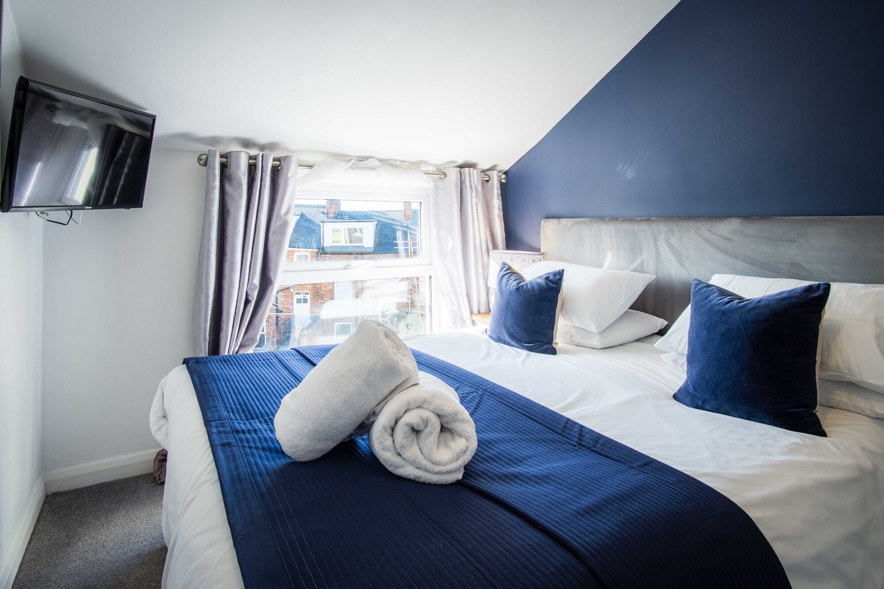 A hotel room with a bed, a TV mounted on the wall, and a window with curtains.