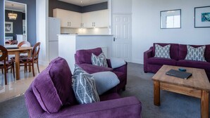 A modern living room with purple sofas, a wooden coffee table, and a dining area with a wooden table and chairs. - Blue Horizon Apartments at The Helaina (Scarborough)
