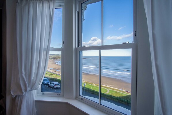 A room with a large window overlooking a beach and ocean.