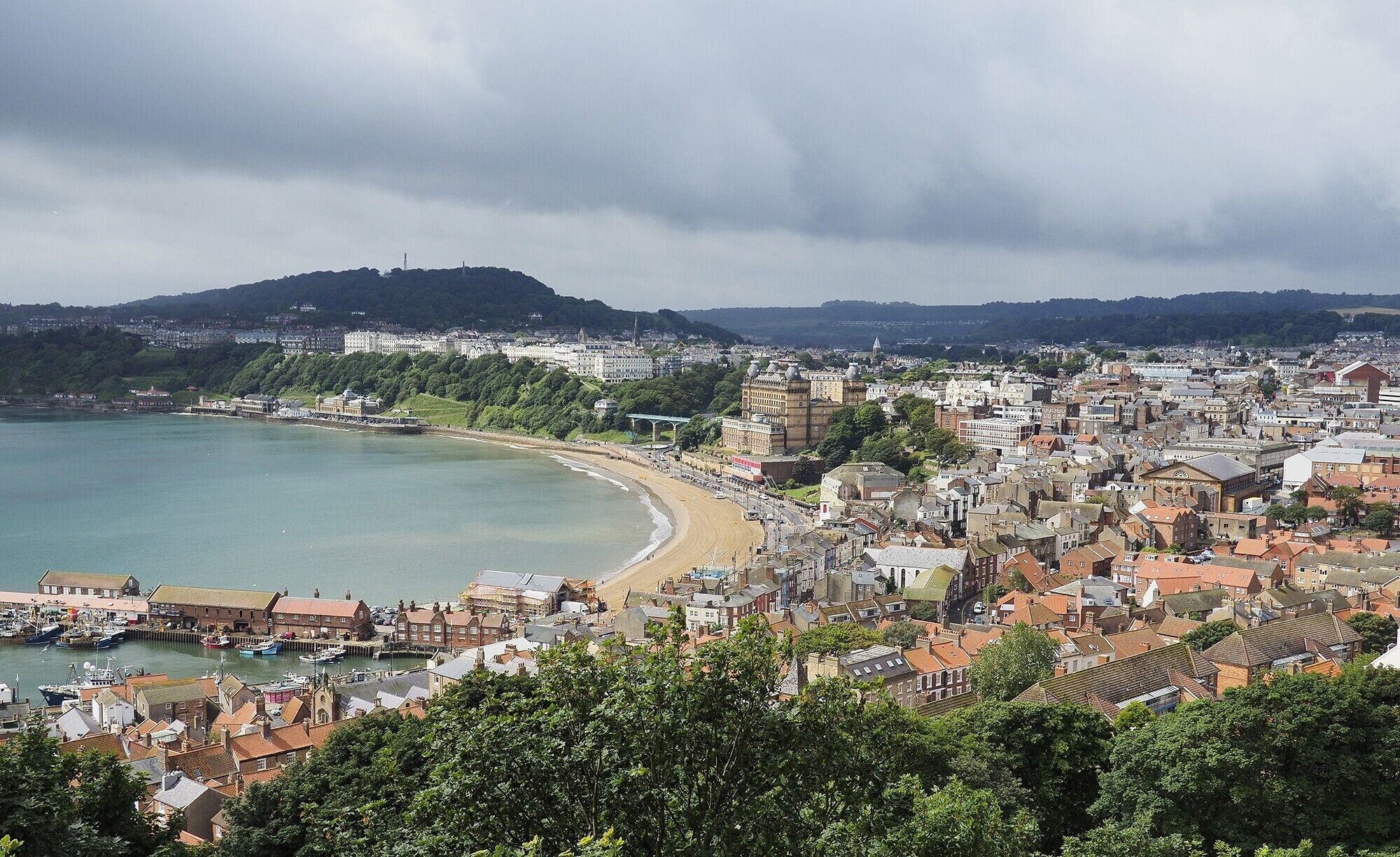A coastal town with a beach, buildings, and a hill in the background.