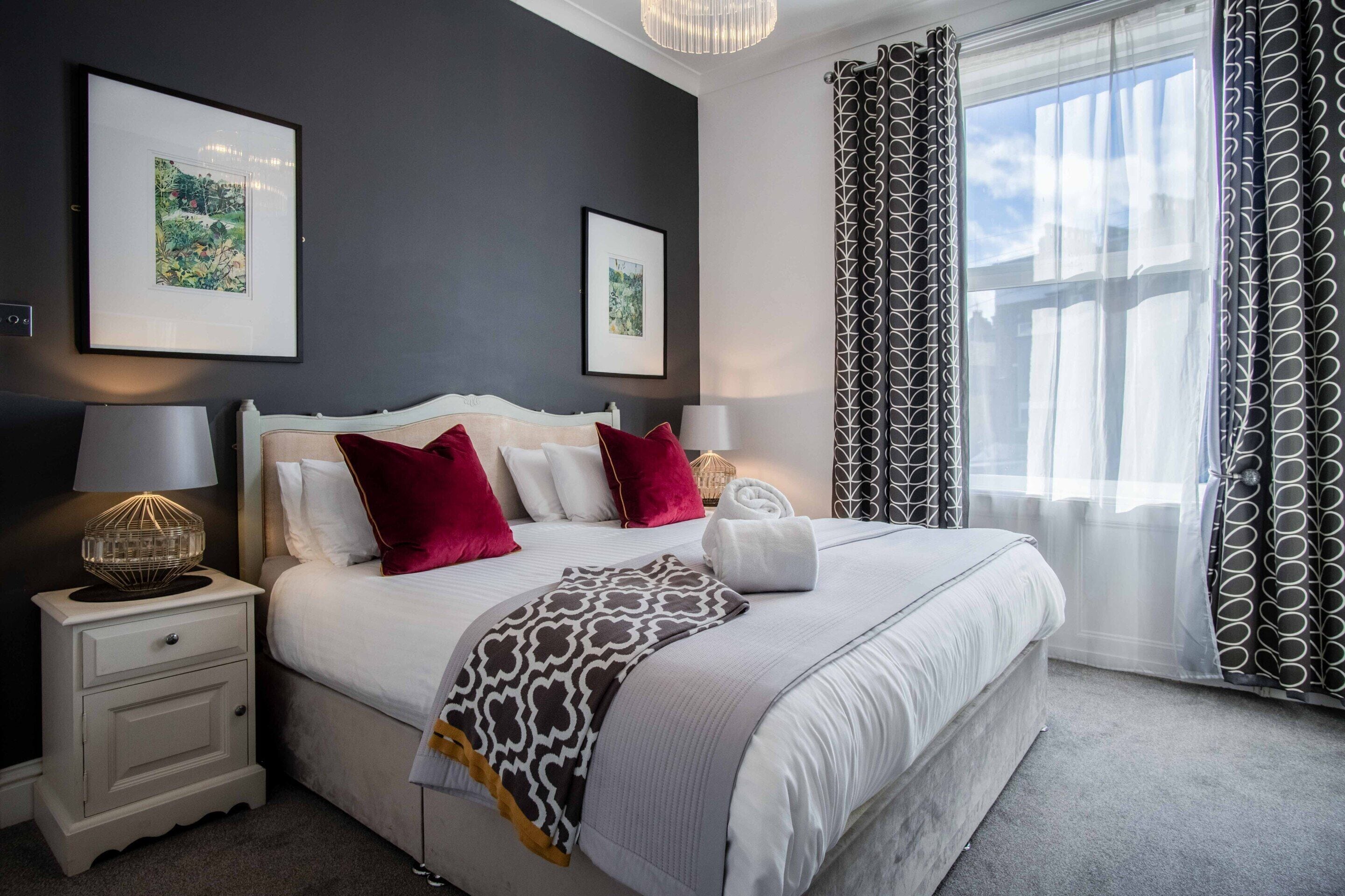 A neatly arranged bedroom with a large bed, two bedside tables, a lamp, and two framed pictures on the wall.