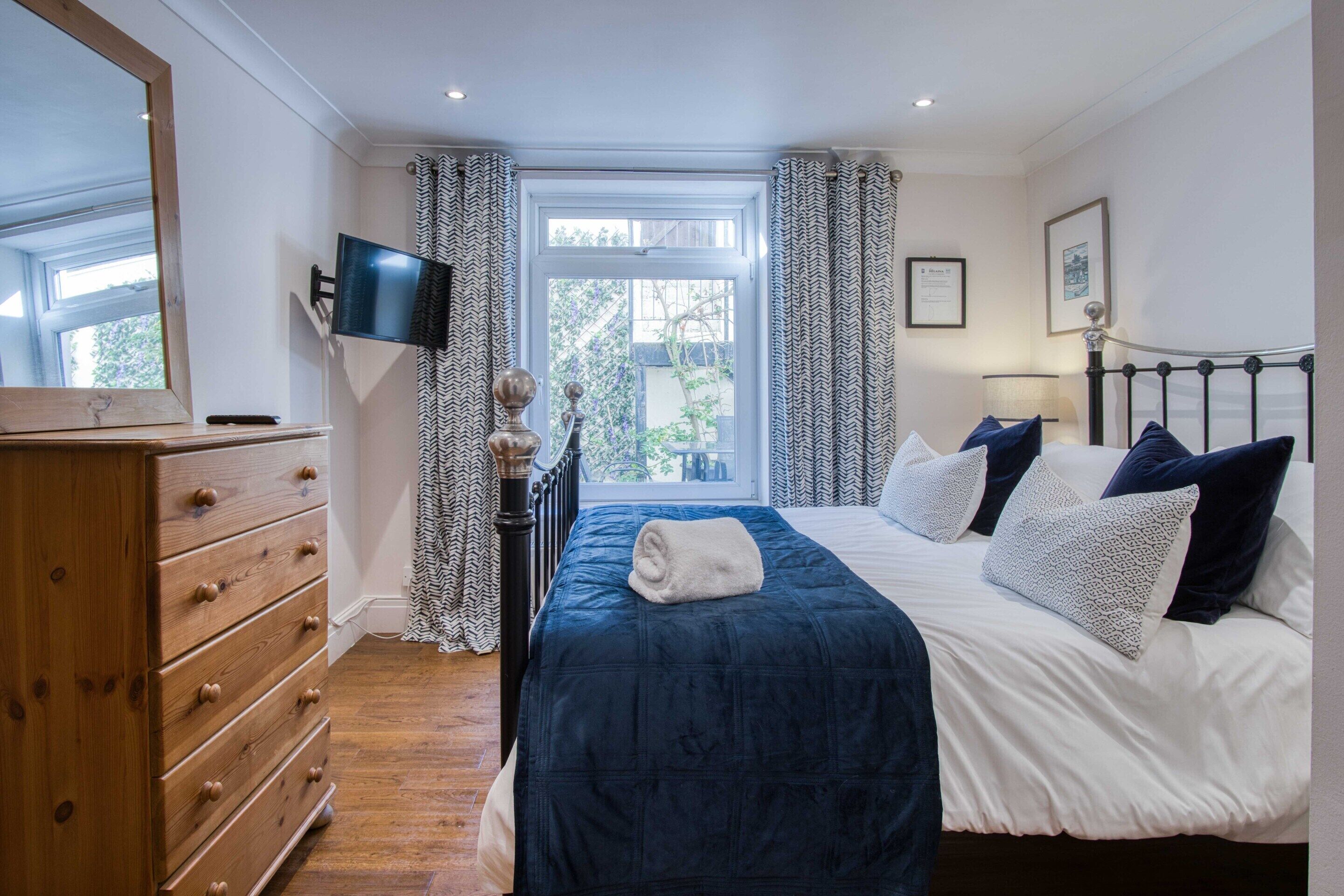 A bedroom with a bed, a dresser, a TV, and a window with curtains.