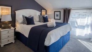 A neatly made bed with a white headboard and navy blue bedding, a bedside lamp, and a small nightstand with drawers. - Blue Horizon Apartments at The Helaina (Scarborough)