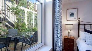 A bedroom with a bed, bedside table, lamp, and a window with a view of a staircase and greenery outside. - Blue Horizon Apartments at The Helaina (Scarborough)