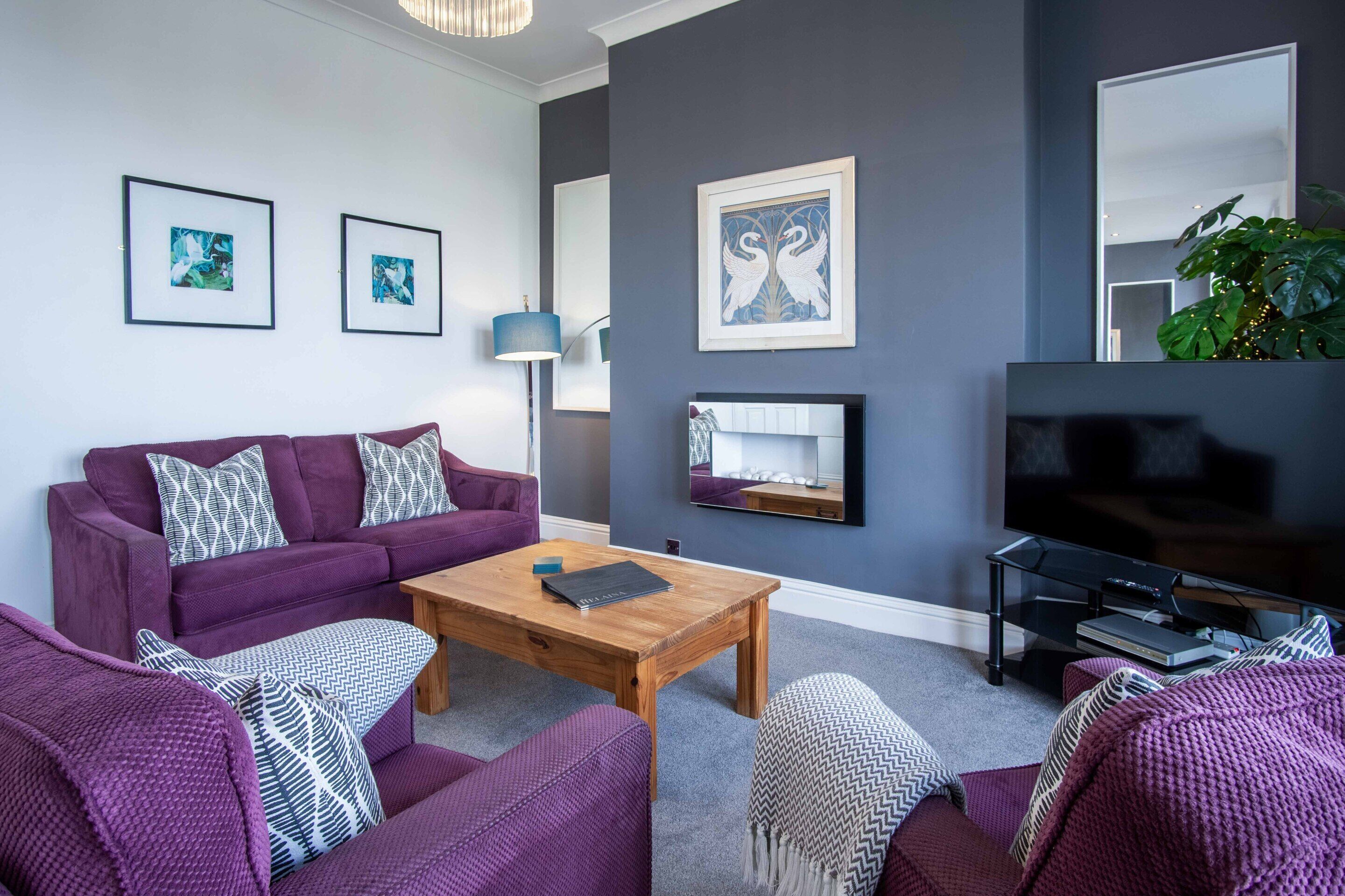 A modern living room with a purple sofa set, a wooden coffee table, and a flat-screen TV.