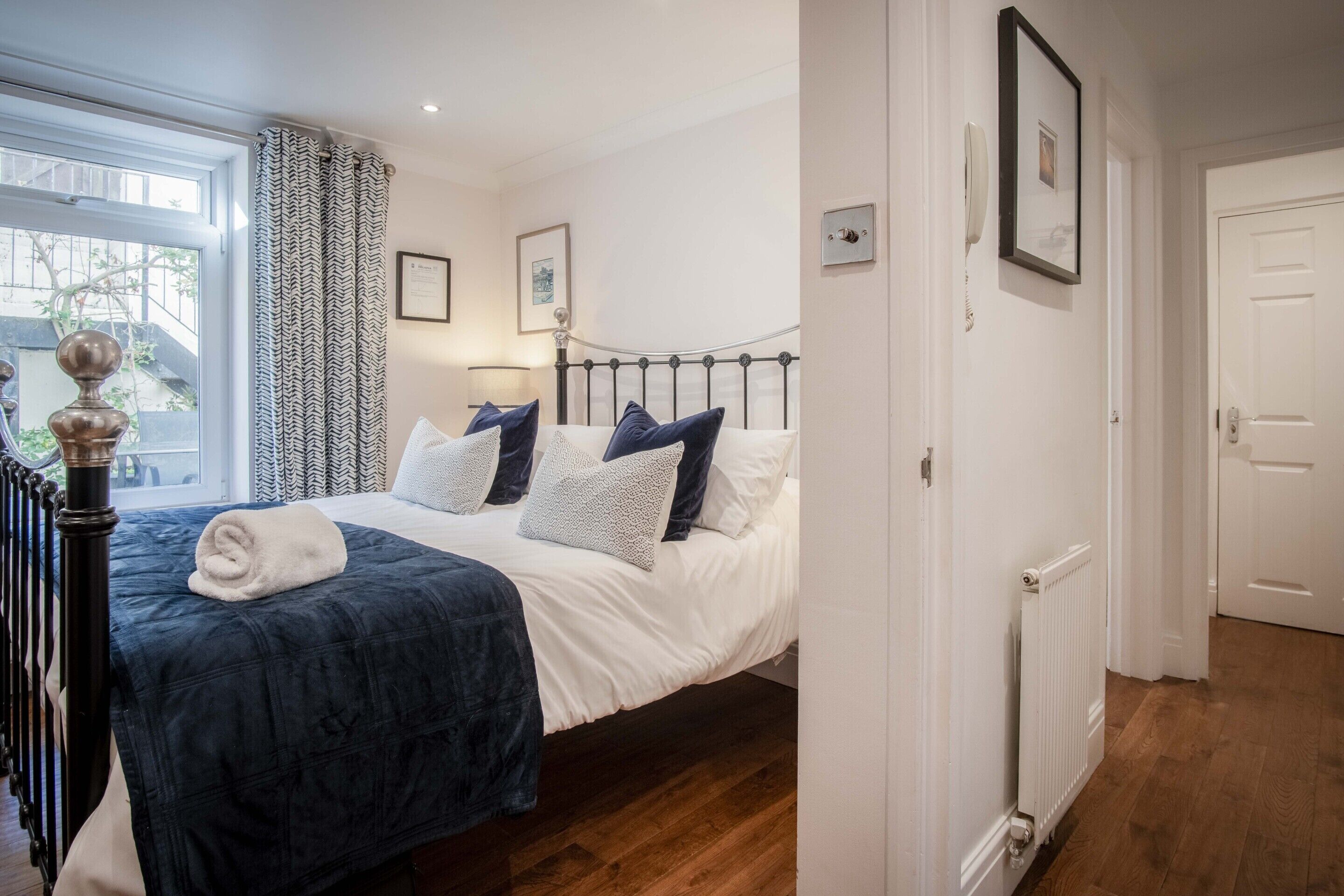 A bedroom with a bed, a radiator, a window with curtains, and a door.