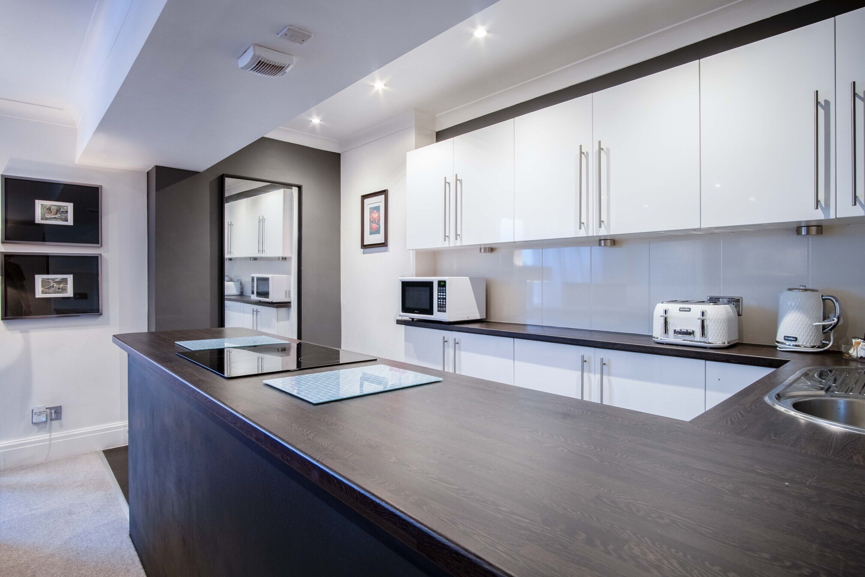 A modern kitchen with white cabinets, a dark countertop, a microwave, a toaster, and a coffee maker.