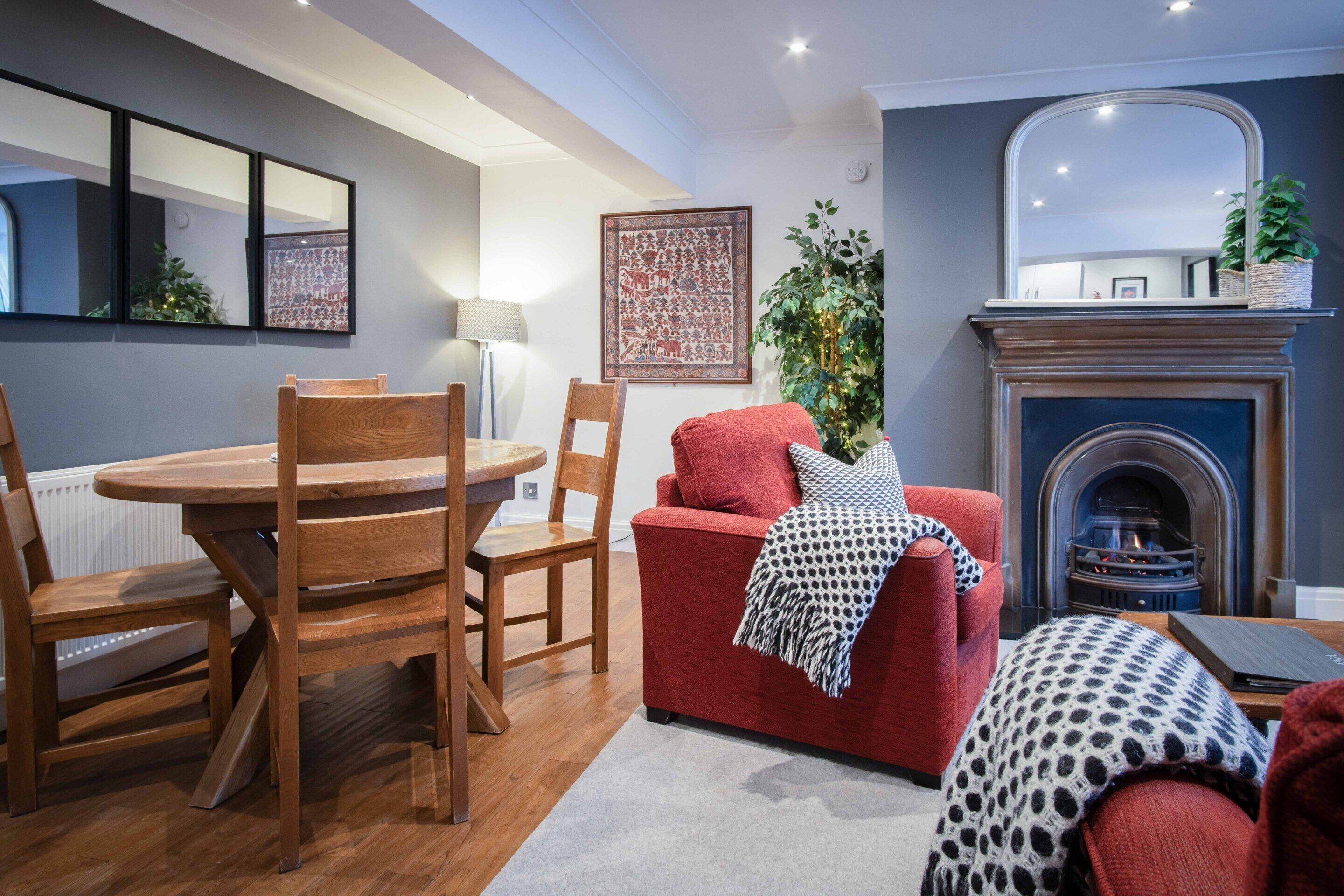 Una sala de estar moderna con un sofá rojo, una mesa de comedor de madera y sillas. Se observa una chimenea al fondo.