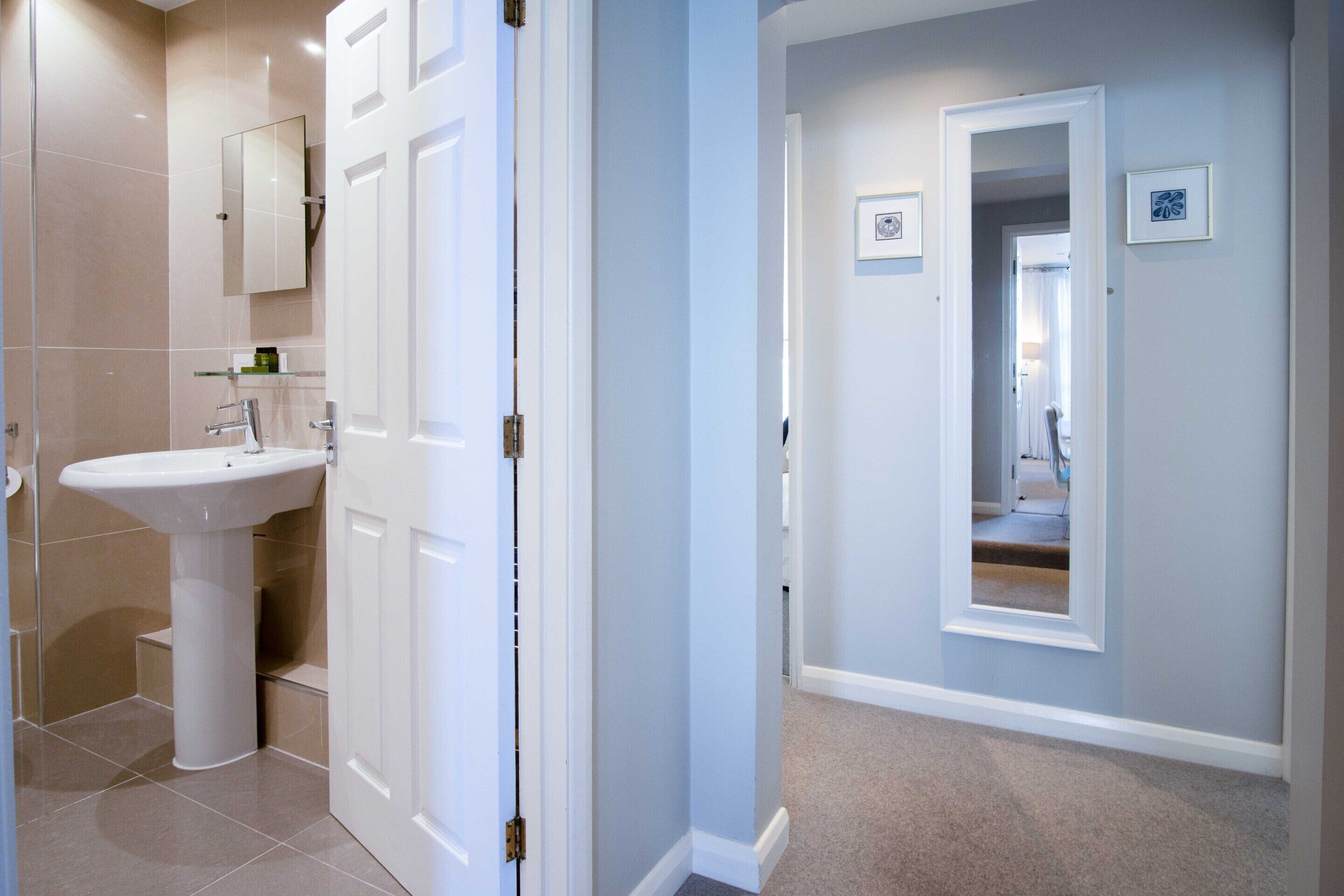 A bathroom with a white pedestal sink, a mirror, and a door leading to another room.