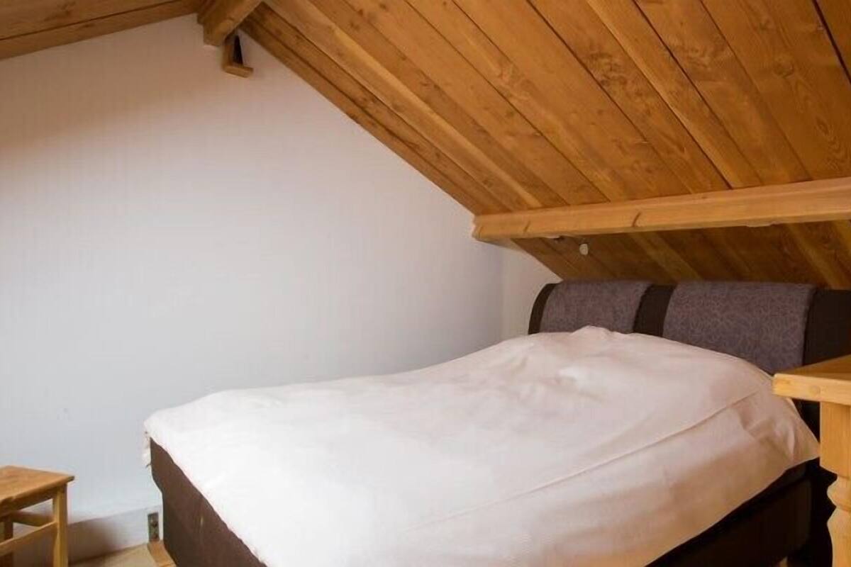 A single bed with a wooden headboard in a room with sloped wooden ceilings.