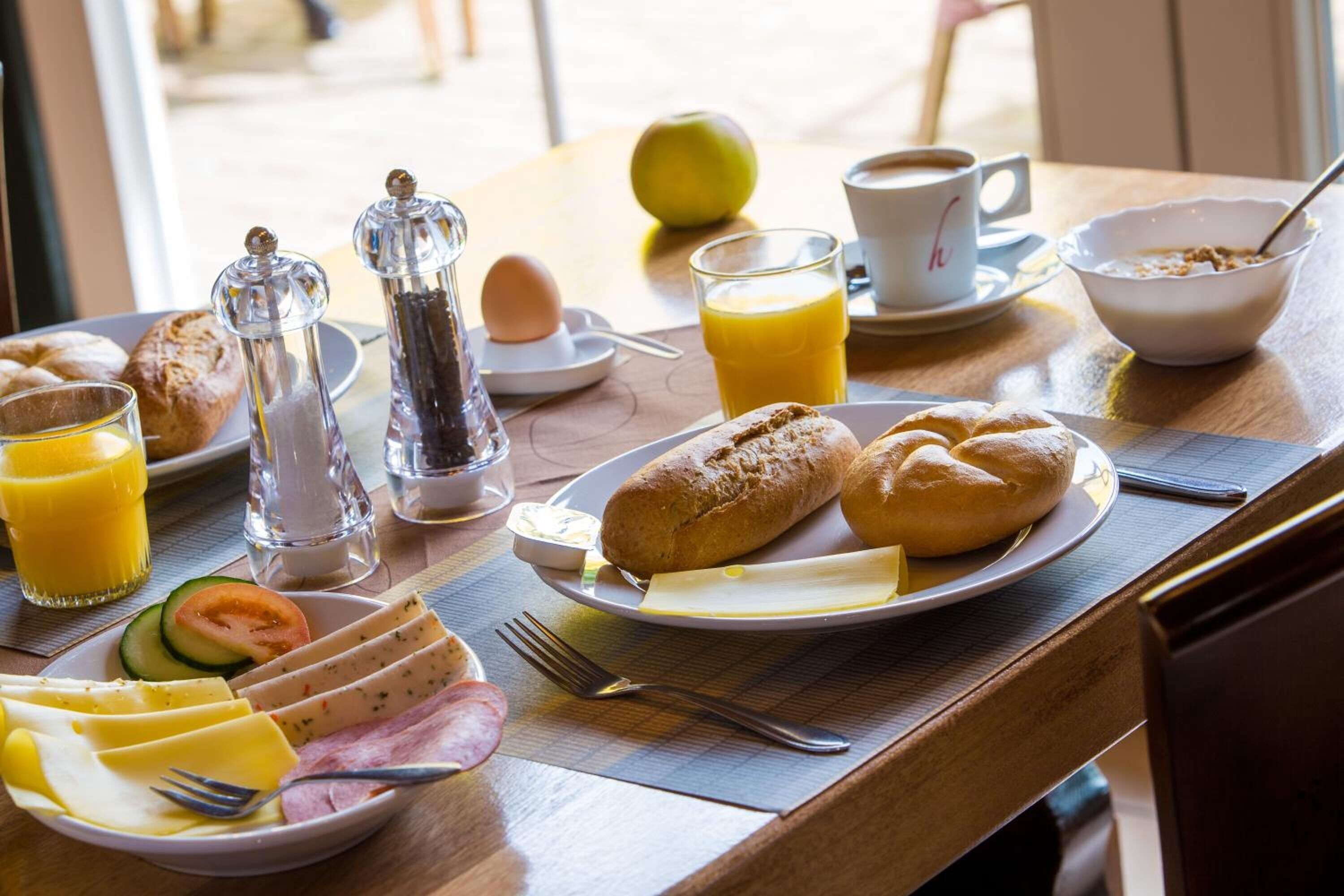 Ein Frühstückstisch mit Croissants, Käse, Schinken und einem Glas Orangensaft.
