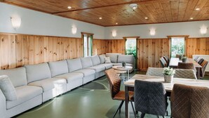 Un interior moderno con techo de madera, un amplio sofá seccional gris, una mesa de comedor con sillas, y una pequeña mesa redonda con una sola silla.