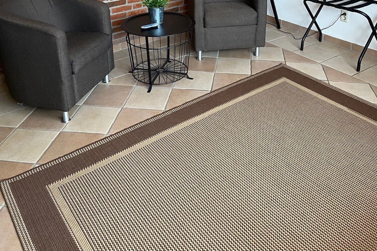 A living room with a brick wall, two armchairs, a small round table with a plant, a floor lamp, and a rug.