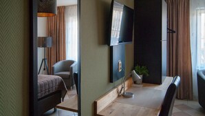 Habitación de hotel con cama, escritorio, silla, televisor montado en la pared y una planta en maceta.